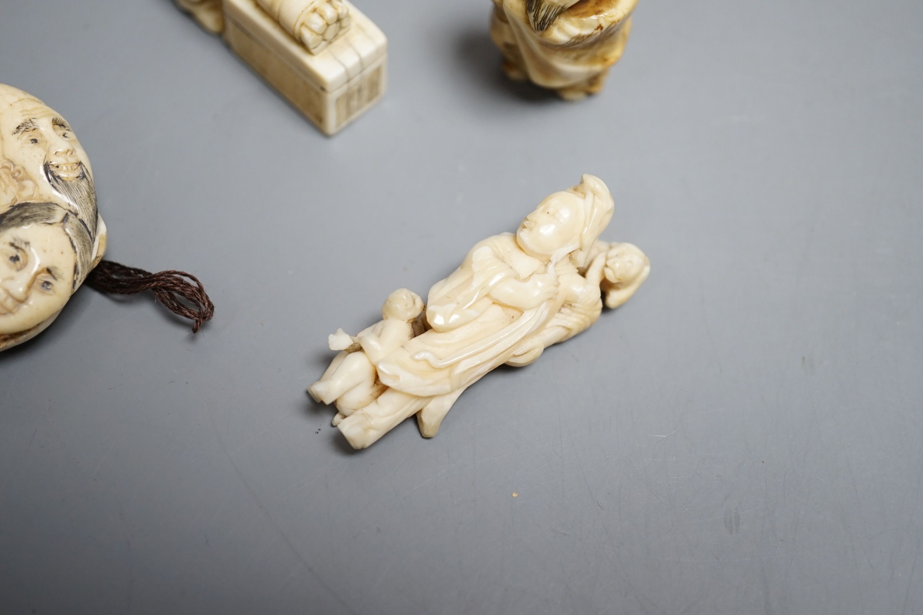 A Japanese ivory netsuke of a man reading a book, a small okimono of Guanyin and monkeys, a Manju netsuke of masks and an early 20th century netsuke of a bearded man